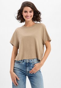 Lichtbruine crop t-shirt met een ronde halslijn, korte mouwen en een losse pasvorm, gecombineerd met lichtblauwe denim jeans.