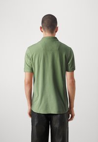 Camisa polo de algodón verde con cuello corto y mangas cortas. Presenta una textura lisa y un detalle de costura en la parte superior de la espalda.
