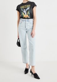 Camiseta negra gráfica con estampado "Más Allá de la Luna", pantalones vaqueros rectos de lavado claro, tacones negros de punta afilada y un pequeño bolso negro.