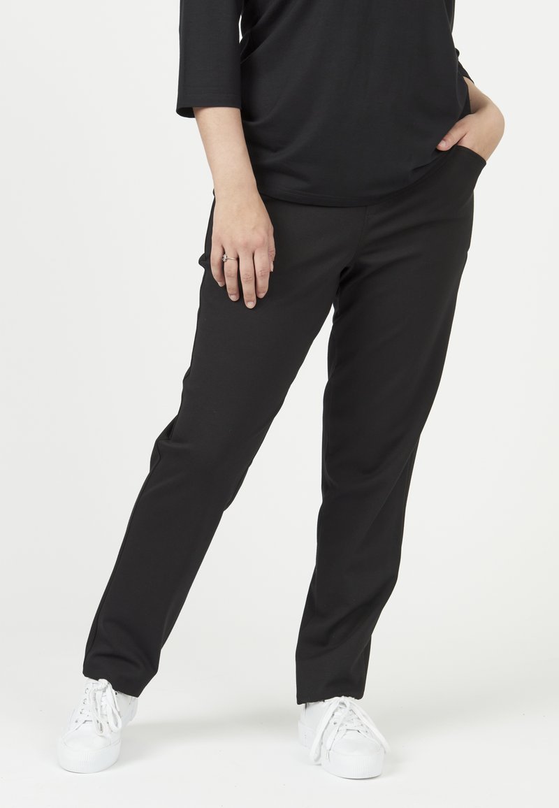 Zwarte slim-fit broek gemaakt van een flexibele stof, met zijzakken en een soepele textuur, gecombineerd met witte sneakers.
