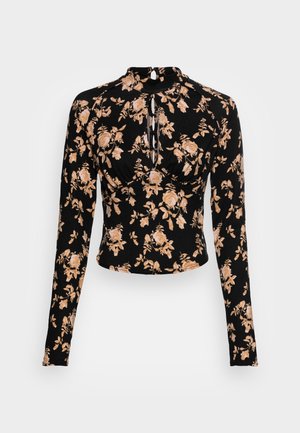 Zwart crop top met lange mouwen, beige bloemenprint, hoge hals, sleutelgat vooraan en gedetailleerde plooien bij de buste.