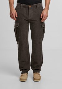 Brązowe spodnie cargo z korduroju, z bocznymi kieszeniami, z zapięciem na guzik i prostymi nogawkami. Nosi się je z beżowymi, teksturowanymi butami.