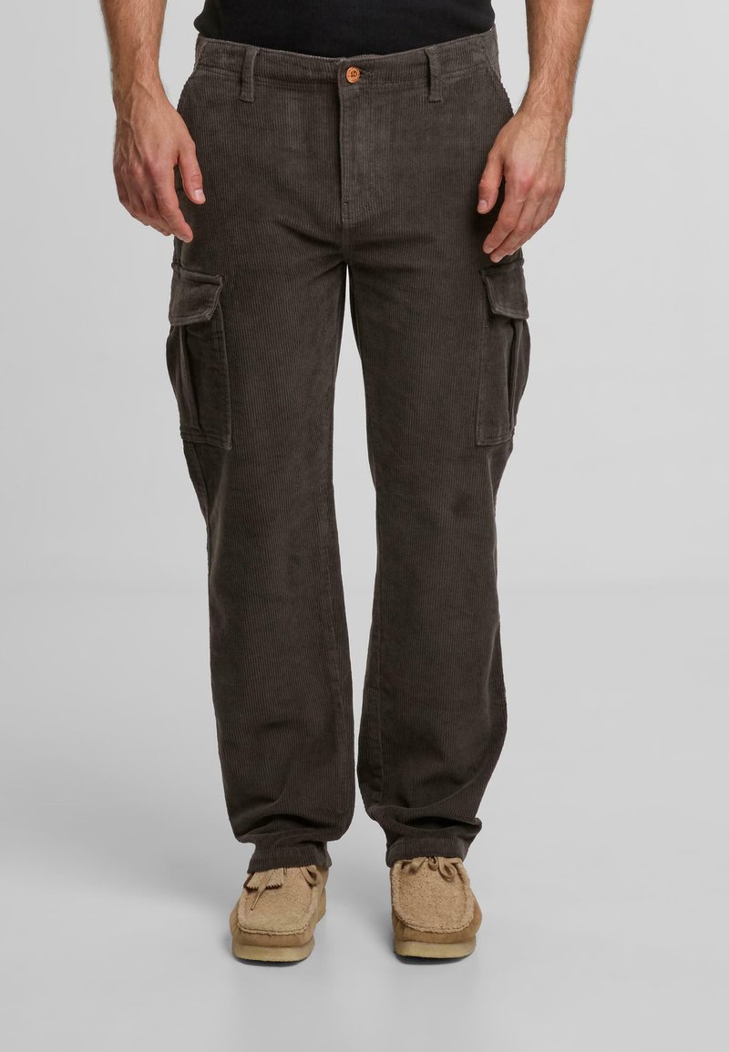 Brązowe spodnie cargo z korduroju, z bocznymi kieszeniami, z zapięciem na guzik i prostymi nogawkami. Nosi się je z beżowymi, teksturowanymi butami.