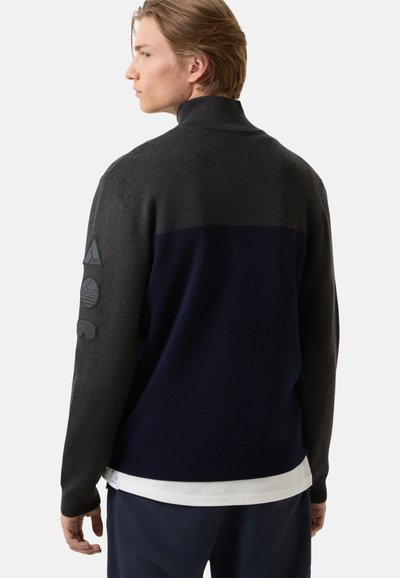 Grau und marineblauer Pullover mit hohem Kragen, strukturiertem Stoff und drei Gummipatches auf dem linken Ärmel. Hat ein tailliertes Design.