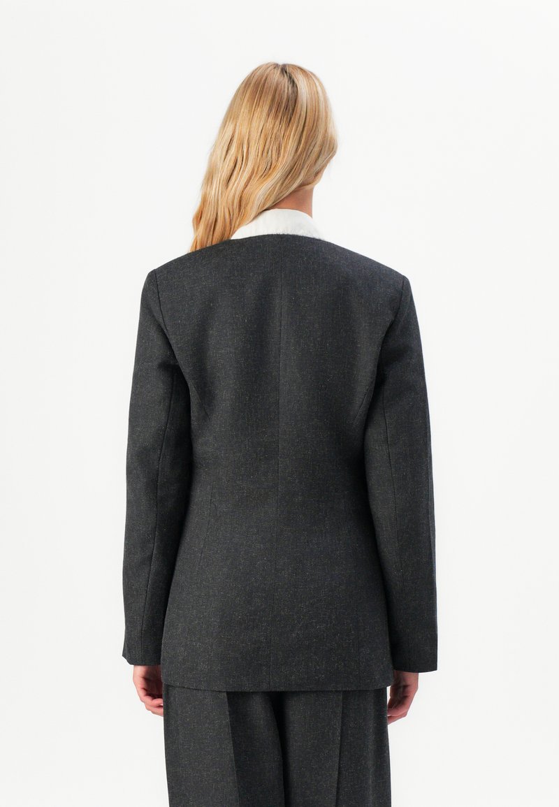 Blazer grigio scuro con un design strutturato, dotato di rever a punta, maniche lunghe e una superficie liscia. La vista posteriore mostra una vestibilità sartoriale e linee pulite.