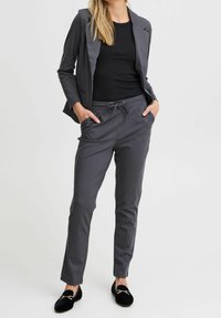 Szara marynarka z dopasowanymi szarymi dresowymi spodniami z sznurkiem w pasie i bocznymi kieszeniami. Cienki czarny top pod spodem, do tego czarne mokasyny.