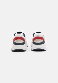 Zapatillas deportivas blancas y marinas con acentos rojos, que presentan un parte superior texturizada, un collar acolchado y una suela blanca más gruesa con la marca en el talón.