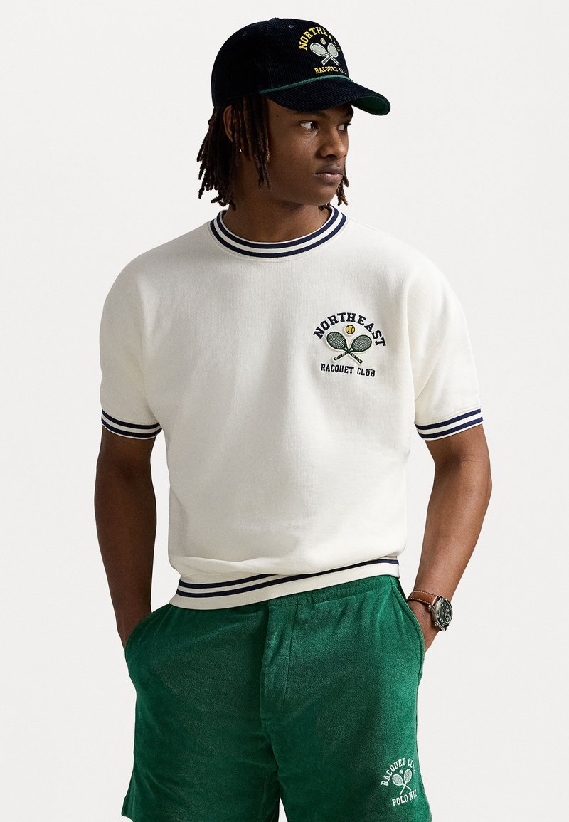 Hvit kortermet genser med marineblå ribbestrikket krage og mansjetter, med grønn og gul brodert "NORTHEAST RACQUET CLUB" logo. Grønne shorts.