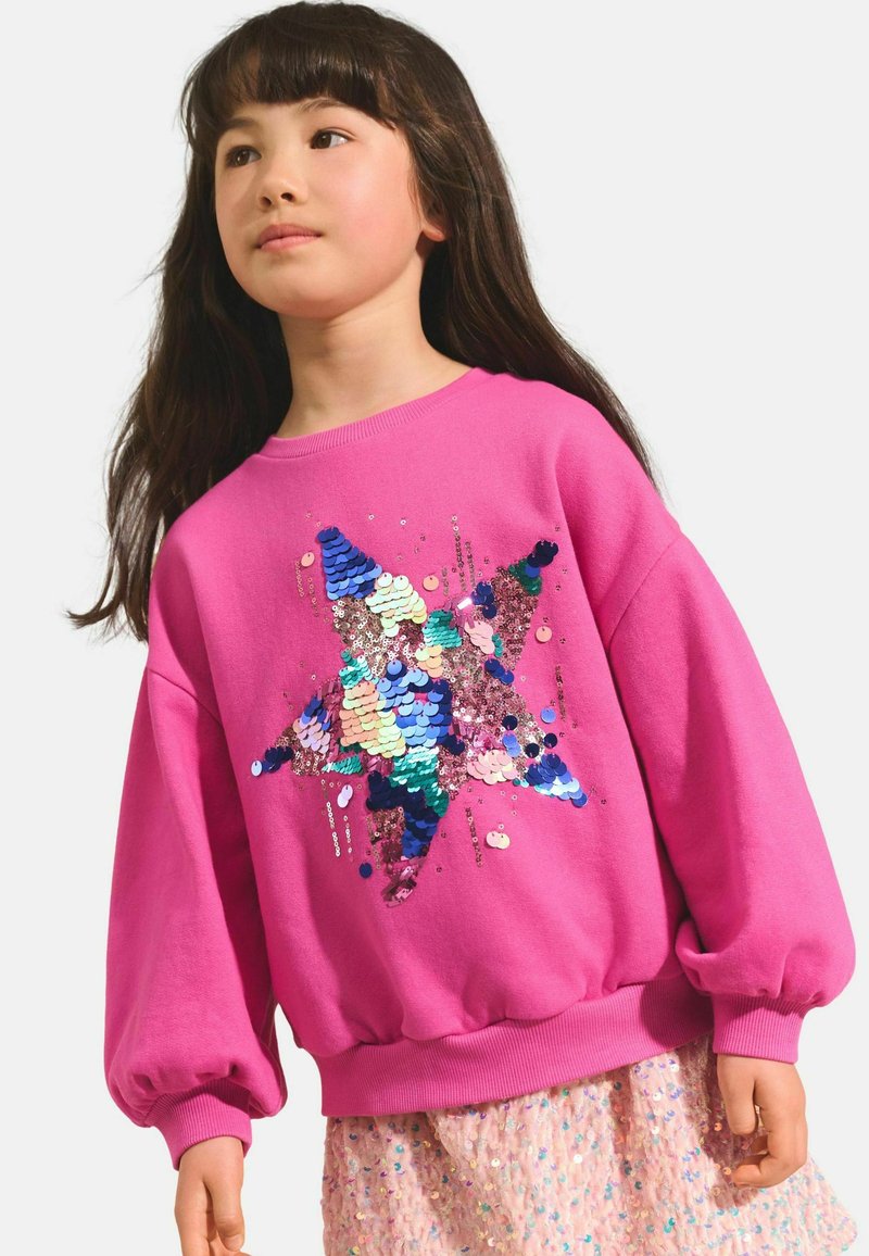 Hanorac roz cu mâneci supradimensionate, având un design cu stea din paiete multicolore. Textură netedă, cu tiv și manșete ribbate.