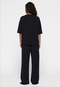 Completo lounge nero con top a maniche corte morbido e pantaloni a gamba larga. Tessuto morbido, cuciture minime e nessun logo o decorazioni visibili.