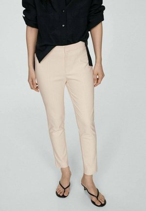 Light pink tailored trousers with a tapered fit, smooth texture, and minimalistic design. Worn with a black button-up shirt and black sandals.