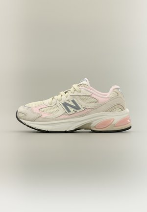 Chaussure de sport New Balance beige clair et rose avec détails en mesh et en suède, semelle rembourrée et logo sur le côté, sur fond neutre.