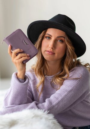 Purple leather wallet with logo detail, held in a hand. Soft, textured fabric sweater in light purple. Black wide-brimmed hat.