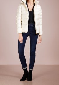 Puffjacka i off-white, med huva, ribbade ärmar och frontdragkedja. Kombinerad med mörkblå jeans och svarta ankelboots.