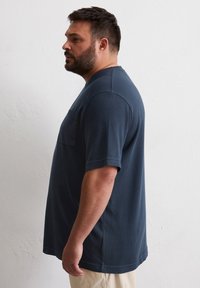 Donkerblauw kortemouwen t-shirt met een rechte snit en een borstzak, gemaakt van zachte katoenen stof, getoond op een mannelijke model.