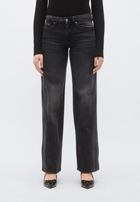 Fekete, széles szárú farmer enyhén kifakult hatással, ötlovas zseb kialakítással és finom steppeléssel. Fekete cipőkkel párosítva, melyeken masni díszítés látható.