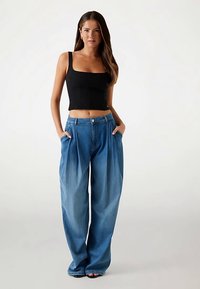 Top nero corto con spalline sottili abbinato a jeans di denim azzurro chiaro, a gamba larga e plissettati; il denim presenta una finitura sbiadita e un design a cinque tasche.