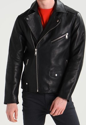 Czarna skórzana kurtka motocyklowa z srebrnymi suwakami i zatrzaskami, noszona na czerwonej koszuli i zestawiona z czarnymi spodniami.