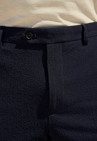 Pantalon texturé bleu marine avec fermeture à bouton à la taille. Tissu tissé à motif quadrillé, finition lisse et coupe ajustée.