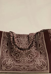 Brązowa torba w stylu bandany z misternym białym wzorem paisley, z miękkiego materiału, z dwoma uchwytami, charakteryzująca się luźnym układem i bogatą teksturą.