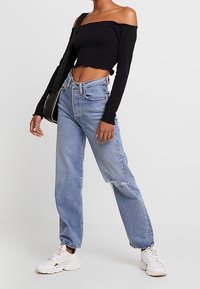 Černý crop top bez ramínek, světle modré džíny s vysokým pasem a roztrhaným detailem, a bílé tenisky. Jednoduchá černá kabelka přes rameno.