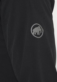 Tissu noir avec une texture lisse présentant un logo circulaire gris proéminent avec un éléphant, positionné sur le haut du bras.