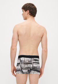 Cuecas boxer masculinas monocromáticas com padrões chamativos do logótipo "DIESEL". Apresentam uma cintura elástica preta e um ajuste justo. O tecido tem uma textura suave.