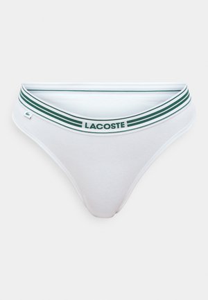 L'intimo bikini bianco in cotone presenta una cintura a strisce verdi con la scritta "LACOSTE" stampata. Texture liscia, design minimalista.