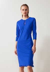 Robe bleu royal en tissu extensible, avec un col rond orné de dentelle au centre et d'une bordure en dentelle à l'ourlet.