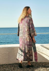 Długi, wzorzysty kimono w żywych odcieniach różu, fioletu i zieleni z szerokimi rękawami, ozdobione misternymi wzorami paisley i bokami z rozcięciami.