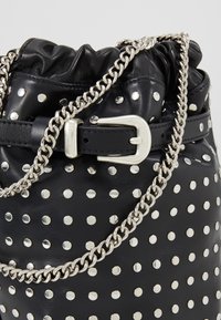 Svart läderhinkväska med silverfärgade nitar, rynkat topp och en silverkedjeslits. Har en justerbar metallspänne.