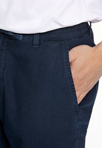 Pantalones chinos de color azul marino con una textura suave, cinturilla elástica y bolsillos laterales. La tela parece ligera y de diseño casual.