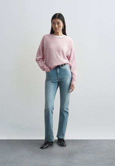 Suéter de malha rosa claro com mangas compridas, combinado com jeans de perna reta azul claro e sapatos pretos. Design simples, com toques mínimos.