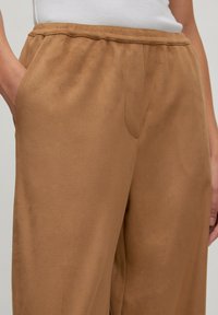 Bruine, suede-achtige broek met een ruime pasvorm, een elastische tailleband en zijzakken. Gladde textuur met een lichte glans.