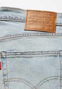 Poche arrière d'un jean en denim bleu clair avec un patch en cuir marron Levi Strauss & Co. affichant le logo de la marque et une étiquette en tissu rouge sur la couture latérale.
