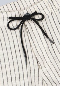 Lightweight fabric pants featuring vertical black and white stripes, a black drawstring closure, and a button at the waist for secure fastening.