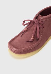 Sapato de camurça roxo com biqueira arredondada, adornado com atacadores e pequenas contas, emparelhado com uma sola de borracha bege flexível.