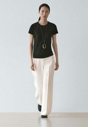 Svart t-shirt med korta ärmar kombinerad med vida byxor i krämfärg, accentuerad med ett långt guldhalsband med hänge. Mjukt tyg, minimalistisk design.