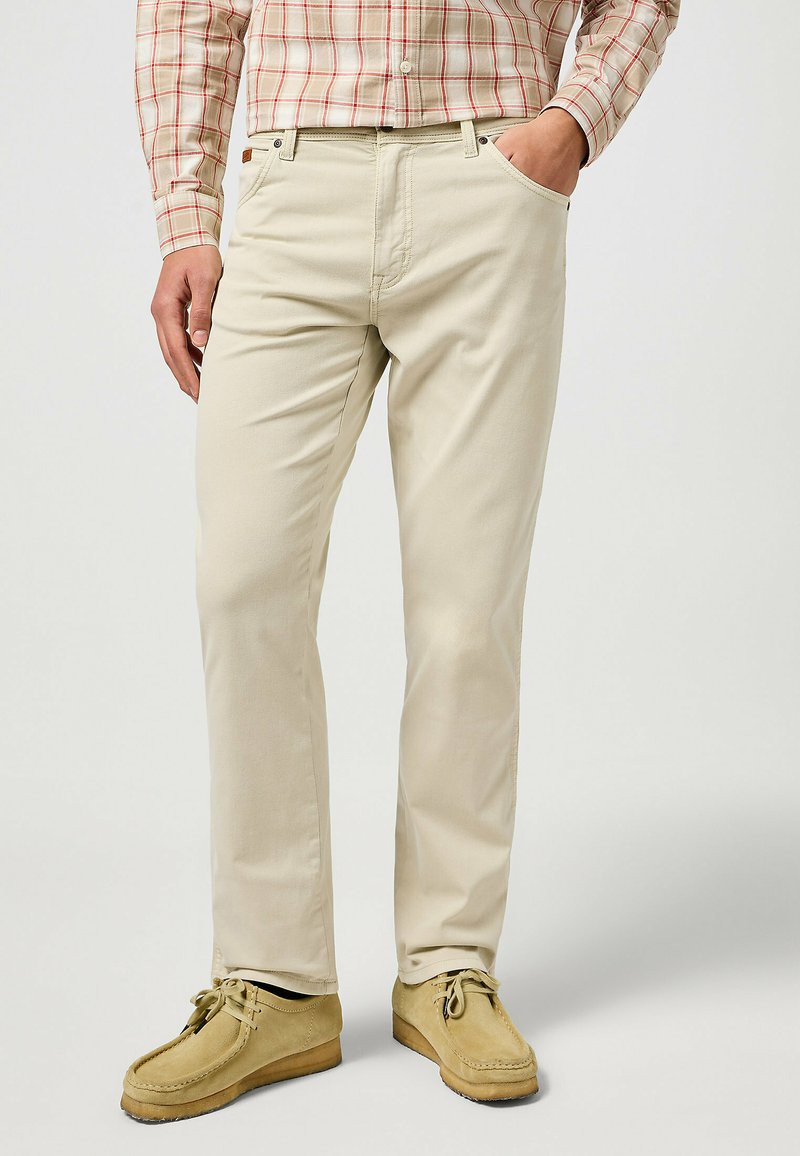 Los pantalones de algodón beige presentan un diseño de pierna recta, bolsillos frontales y una textura suave, combinados con zapatos estilo mocasín de color beige claro.