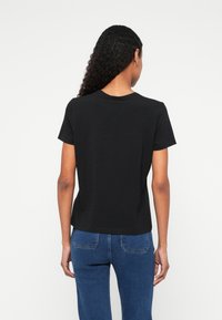 Tricou negru din bumbac cu mâneci scurte, guler rotund și croială lejeră, asortat cu blugi albaștri din denim cu buzunare la spate.