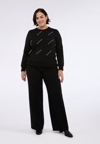 Felpa nera con motivo a diamante e dettagli argentati, abbinata a pantaloni neri a gamba larga e scarpe nere, con una texture liscia.