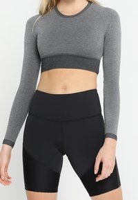 Graues langärmliges Cropped-Top mit geripptem Saum; kombiniert mit hoch taillierten schwarzen Shorts, die über strukturierte Einsätze und eine glatte Oberfläche verfügen.