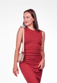 Červené šaty bez rukávů s těsným střihem a žebrovanou texturou. V kombinaci s malou světle béžovou kabelkou přes rameno s prošívaným vzorem.