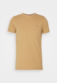T-shirt à manches courtes, col rond en coton brun clair. Doté d'un petit logo sur la poitrine. Texture lisse, design ajusté.