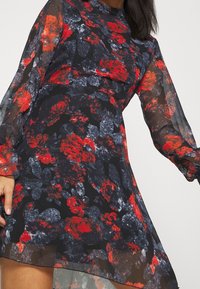 Vestido floral hecho de tela transparente, con un fondo negro y patrones florales en rojo y gris. Mangas largas y fluidas, y una cintura ajustada.