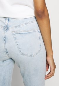 Jeans de mezclilla de color azul claro con una textura suave, cintura alta, dos bolsillos traseros y detalles de costura sutiles. El ajuste es ceñido en las caderas.