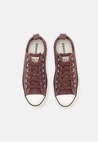 Baskets en toile bordeaux avec bouts en caoutchouc blanc, lacets plats et coutures contrastées. Présente un patch logo sur la languette et un onglet au talon.