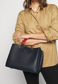 Granatowa skórzana torebka z różowymi akcentami na uchwytach, srebrnymi detalami i logo. Ustrukturyzowany kształt z przeszytymi bocznymi panelami.