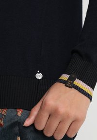 Dunkelblauer Strickpullover mit gerippten Bündchen in Gelb, Pink und Blau sowie einem silbernen Akzent am Saum mit Branding-Details.