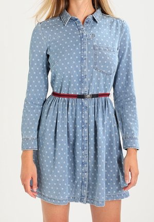 Niebieska jeansowa sukienka w białe kropki, z długimi rękawami, kieszenią na piersi, zapięciem na guziki z przodu oraz wąskim czerwono-czarnym paskiem w talii.